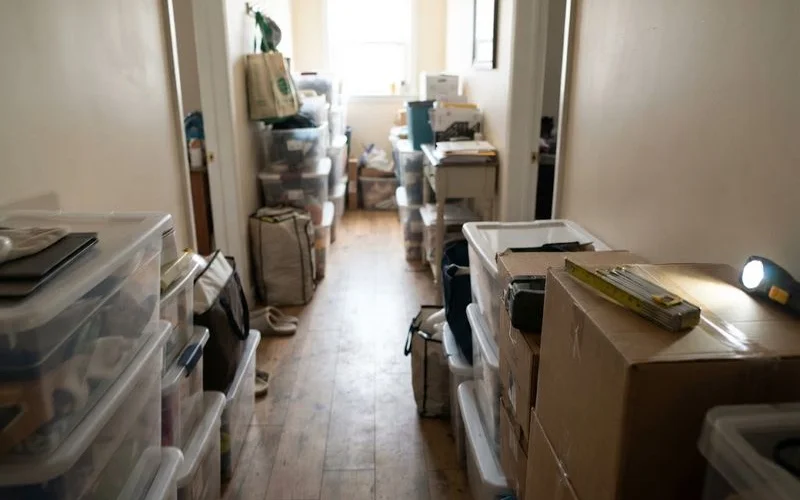 A hallway partially blocked by stacked boxes and belongings, illustrating a blocked exit hazard in a cluttered home
